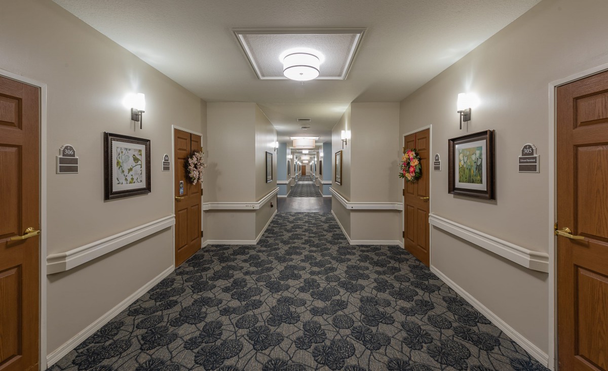 A well-decorated hallway with patterned carpet, artwork on the walls, and bright lighting.