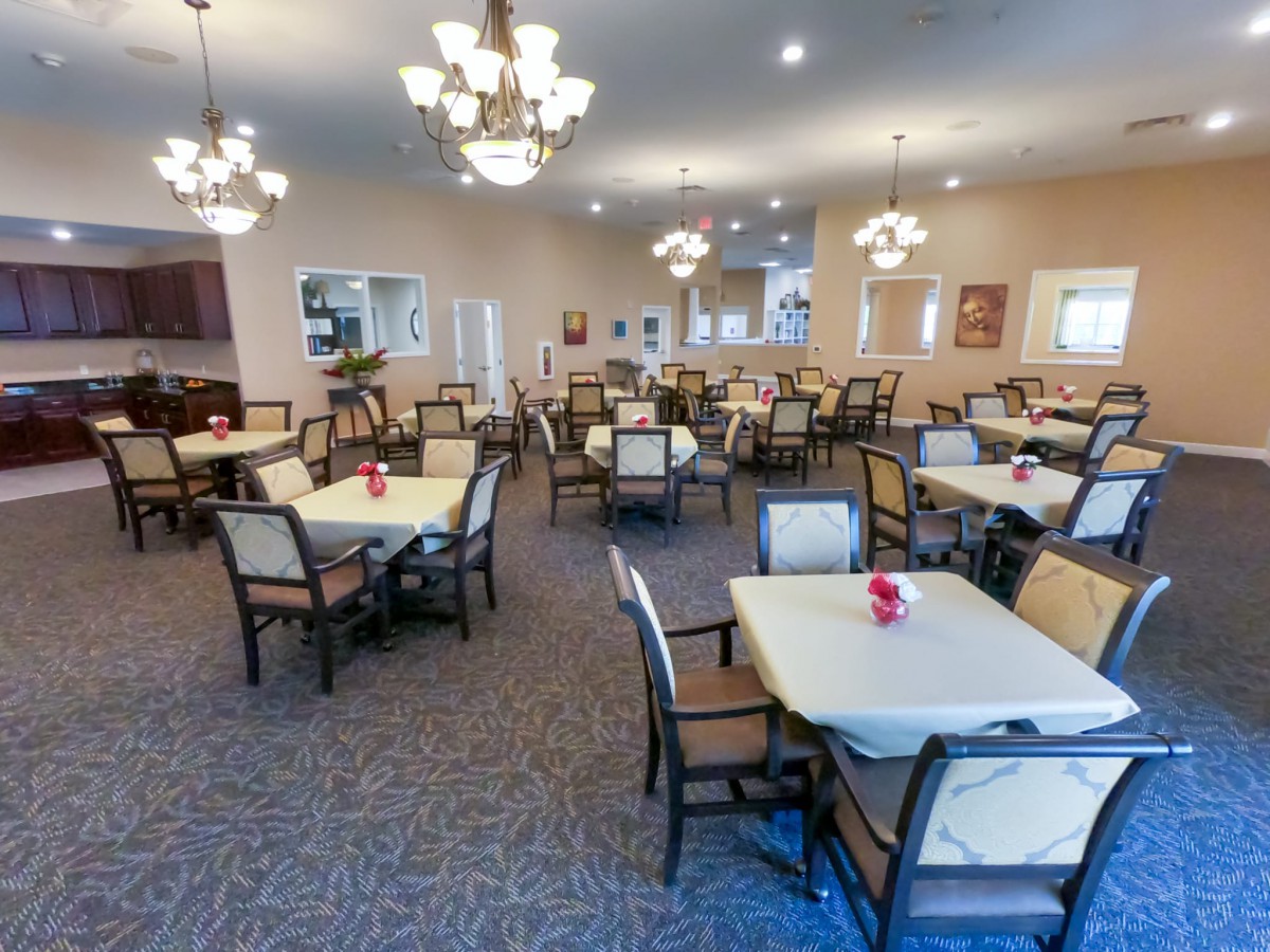 A spacious dining room with neatly arranged tables and chairs, illuminated by elegant chandeliers.