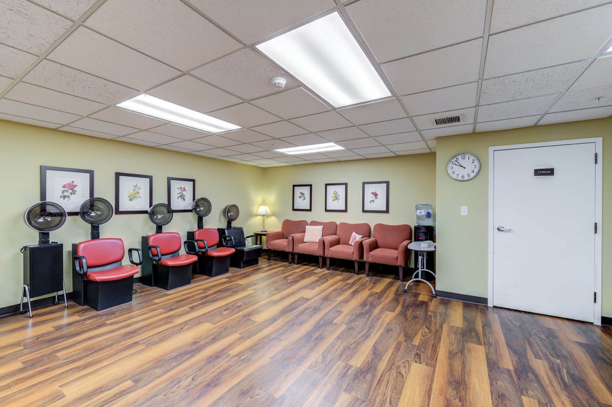 A spacious salon waiting area with hair dryers and seating, featuring a warm wooden floor and decorative wall frames.