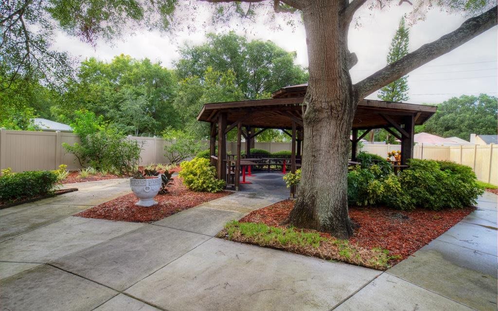 A serene garden area featuring a gazebo surrounded by lush greenery and a large tree.