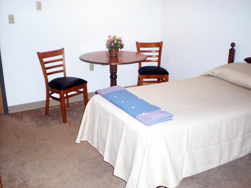A simple bedroom setup with a bed, two chairs, and a small round table.
