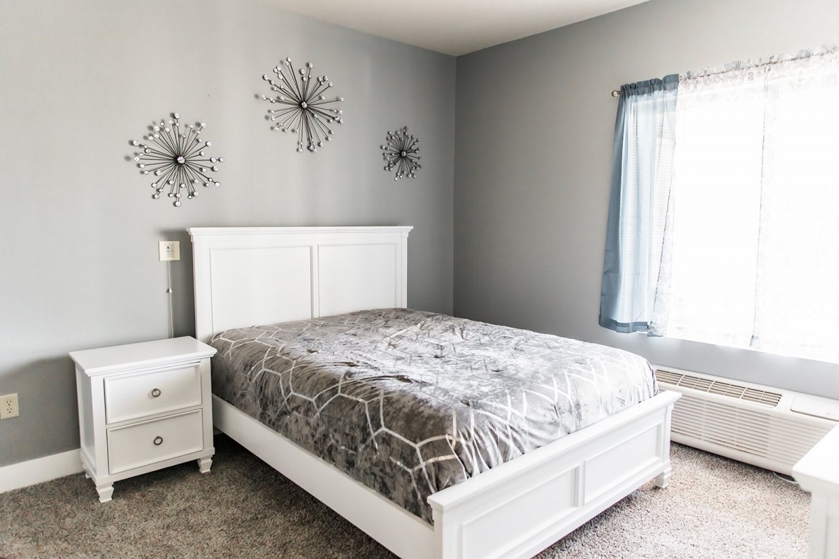 A cozy bedroom with white furniture and minimalist decor, featuring gray walls and decorative wall art.