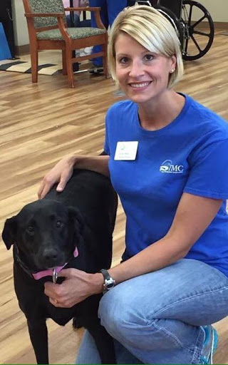 A woman with a big smile poses with a black Labrador dog, showcasing the joy of pet companionship.