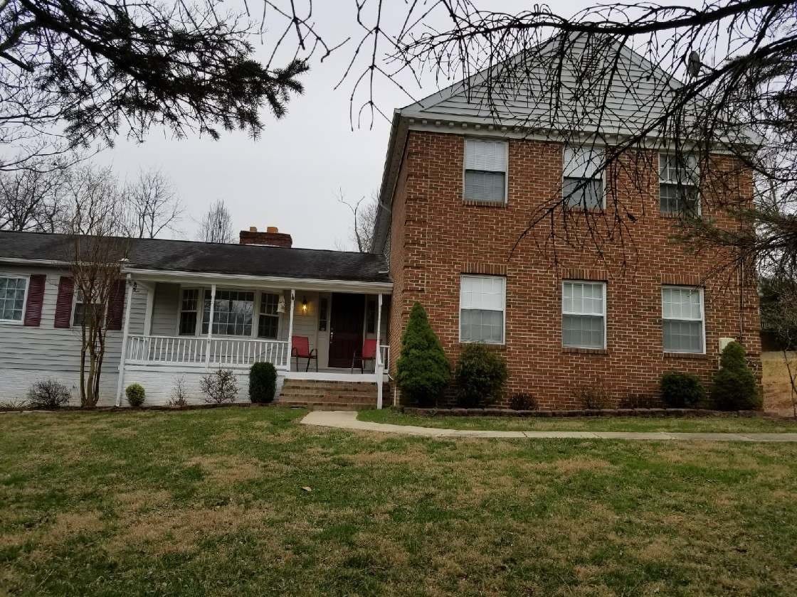 A brick house with a porch and a large lawn in a suburban area.