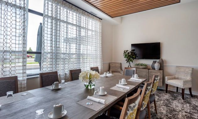 A modern dining room setup with a large table, arranged chairs, and ample natural light from the windows.