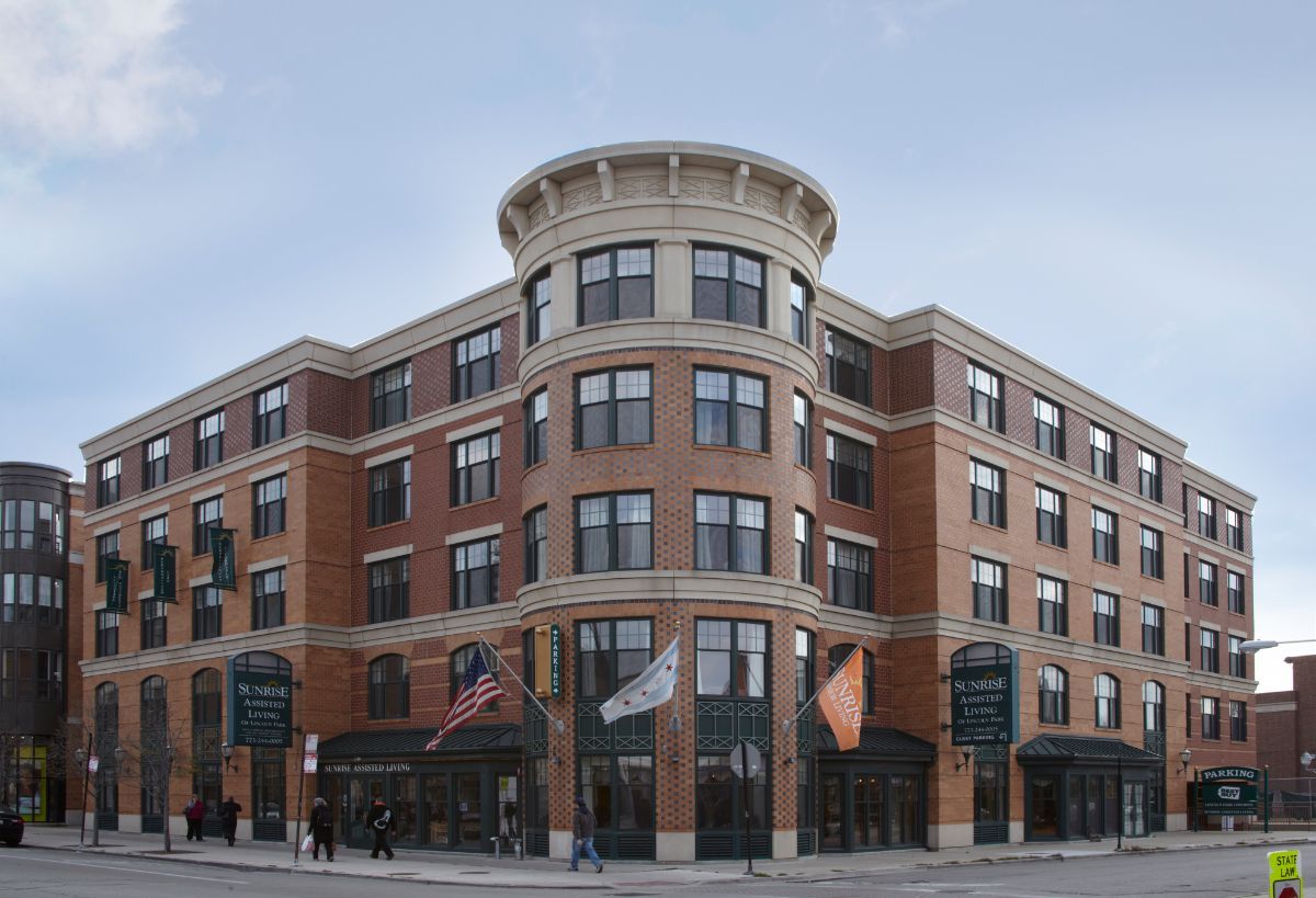 A multi-story brick building with a rounded corner and various flags displayed, situated in an urban environment.