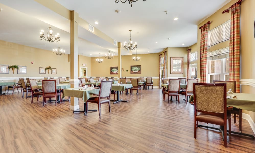 An elegant dining room with neatly arranged tables and chairs, featuring chandeliers and a wooden floor.