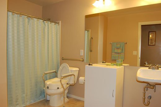 A bathroom with a light blue shower curtain, toilet, sink, and mirror under warm lighting.