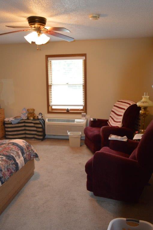 A cozy bedroom with a bed, two armchairs, and a window letting in natural light.
