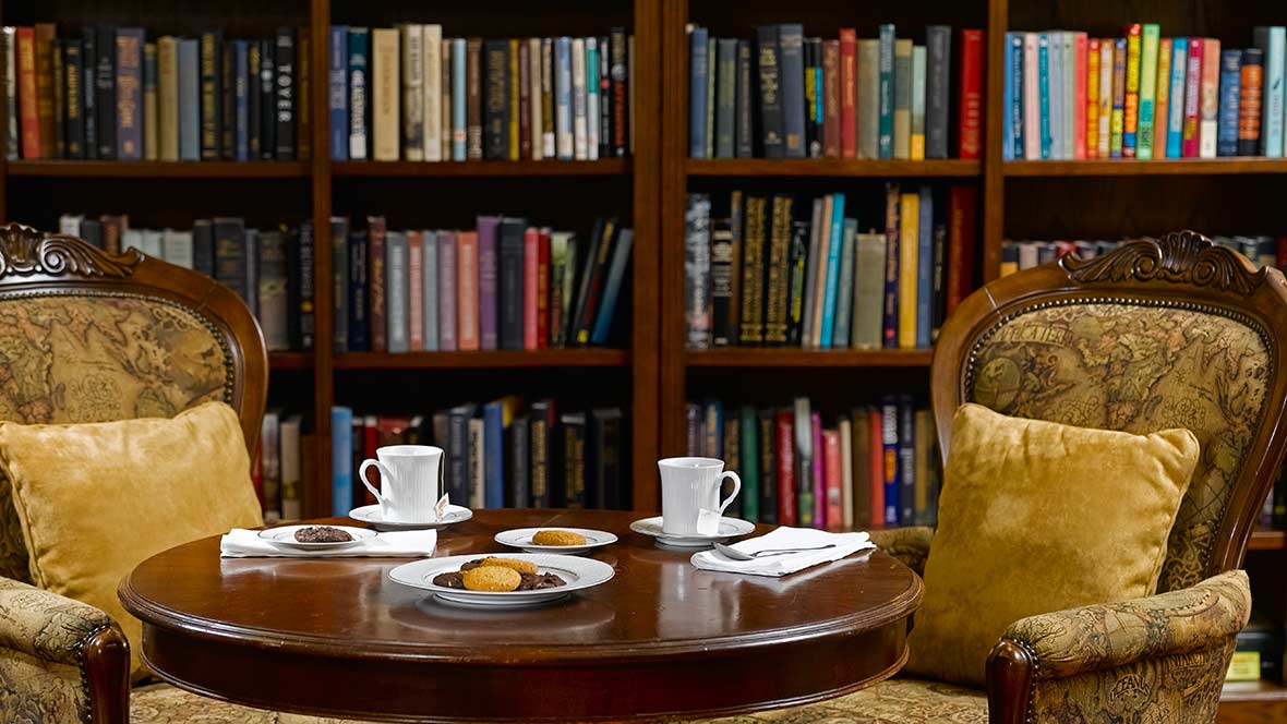 A cozy library setting with tea and cookies on a wooden table.