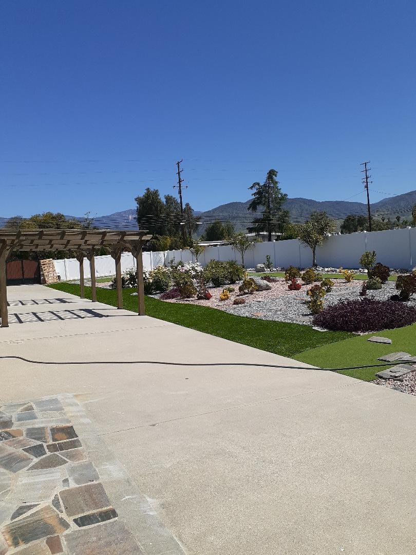 A sunny garden with a pergola, patio, and mountainous backdrop.