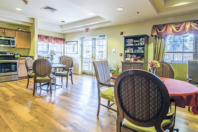 A cozy dining area with wooden floors, several tables and chairs, and natural light streaming through the windows.