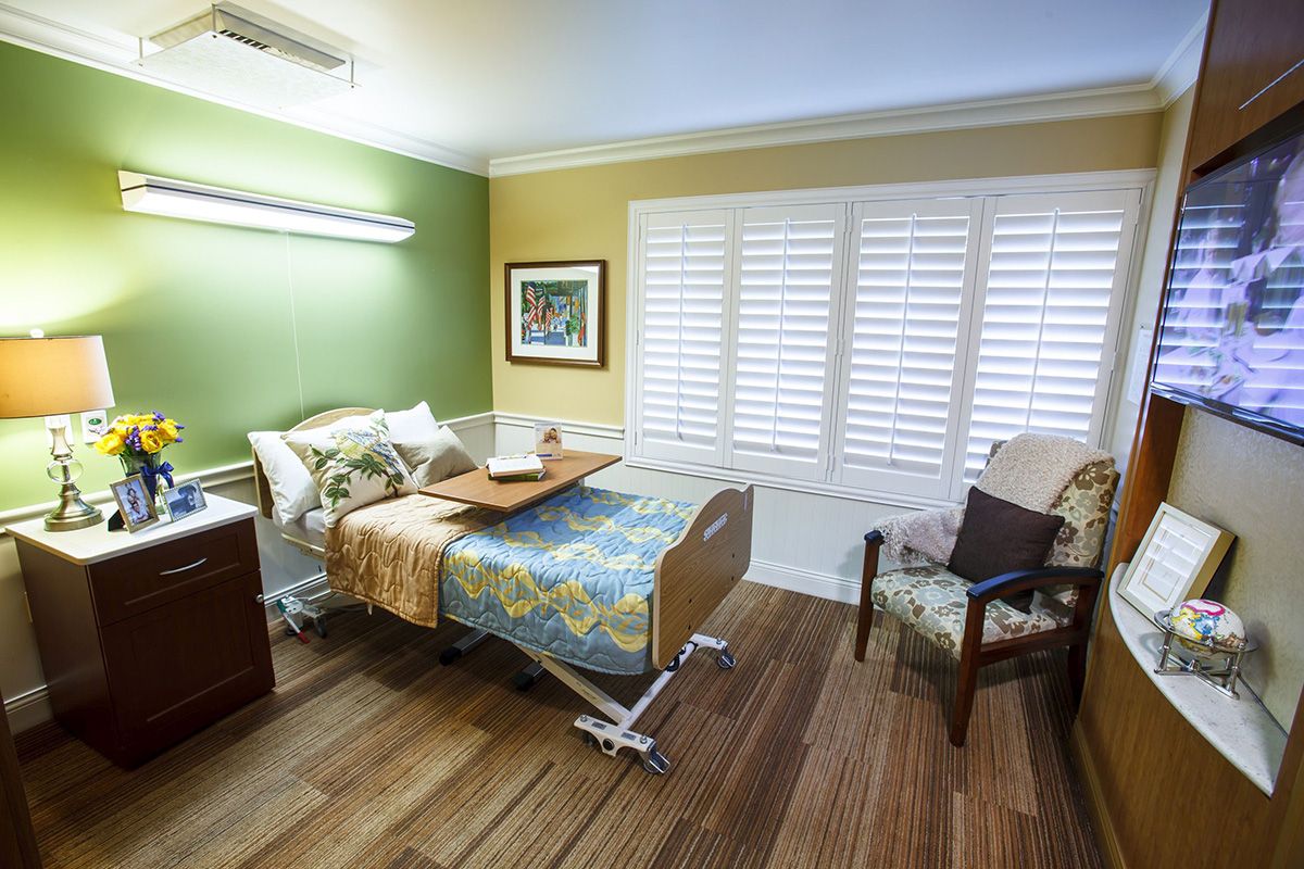 A clean and organized hospital room with a bed and seating area.