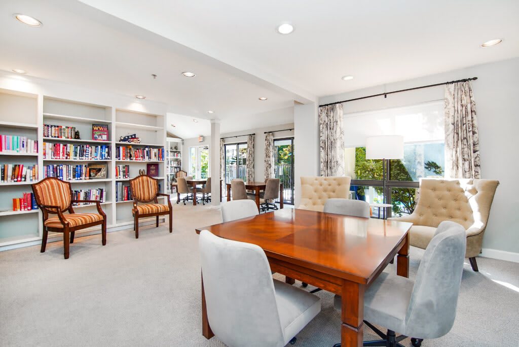 A spacious and well-lit living room with a wooden table, cushioned chairs, and bookshelves.