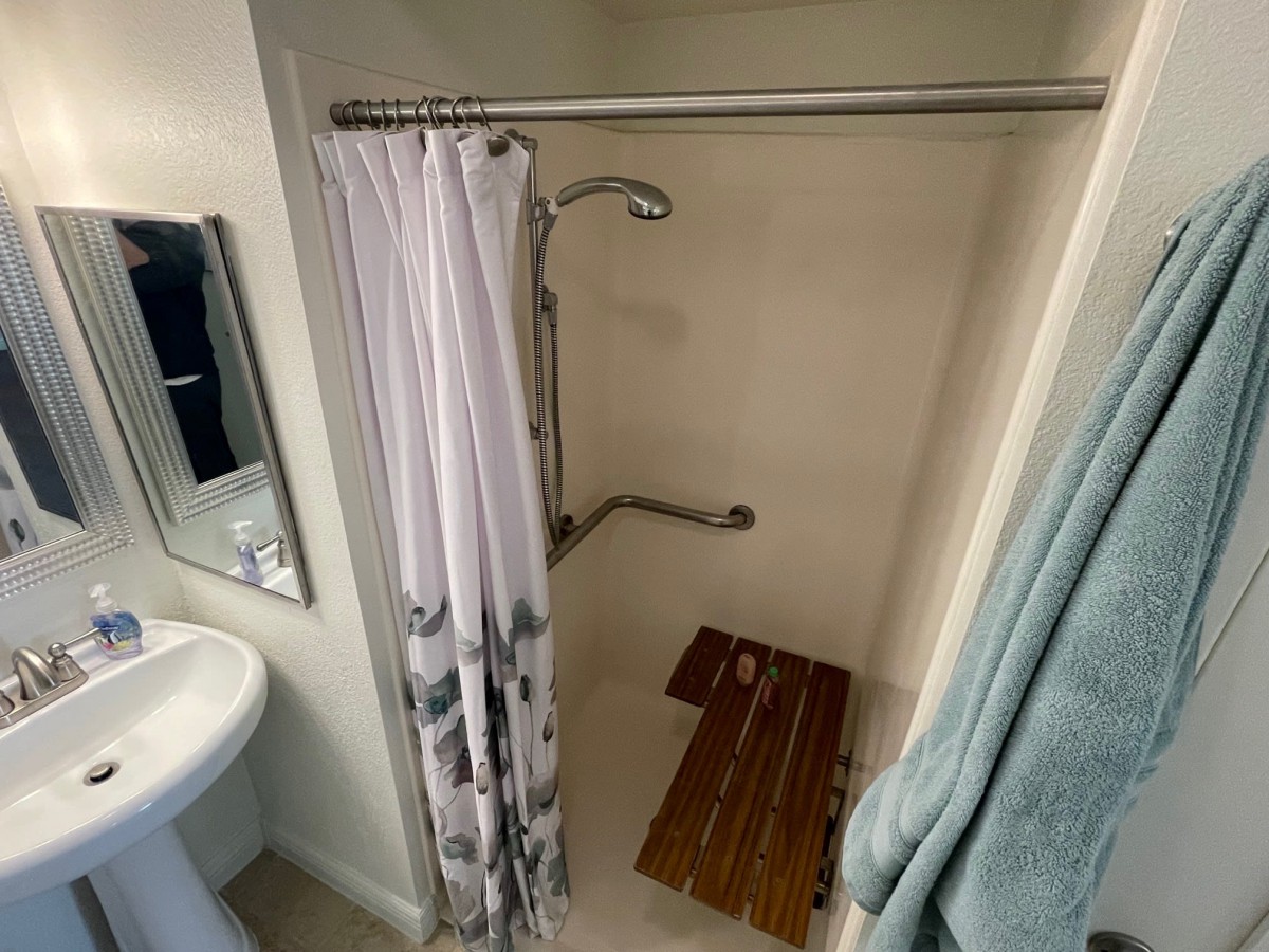 A small bathroom featuring a shower with a curtain and bath mat, adjacent to a sink and mirror.