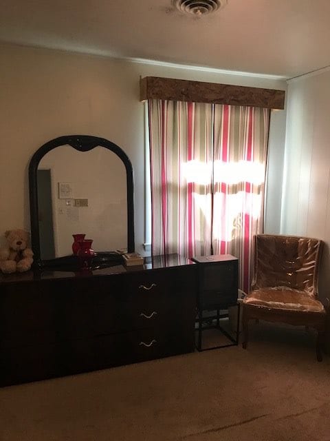 A cozy bedroom corner featuring a dark wooden dresser with a mirror, colorful curtains, and an ornate chair.