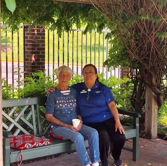 Two people sitting on a bench in a park surrounded by greenery.
