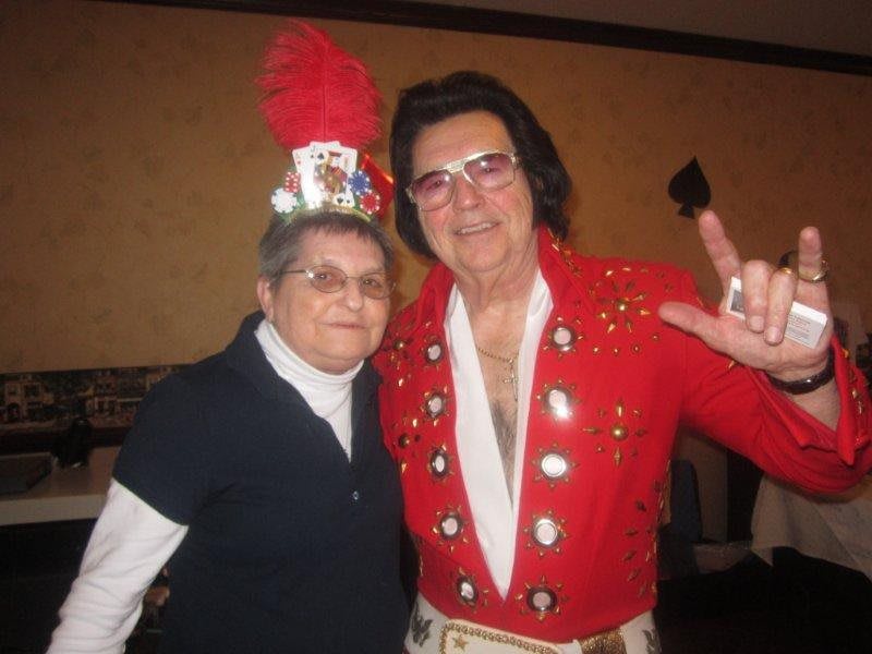 Two people posing together, one dressed as an Elvis impersonator and the other wearing a festive party hat.
