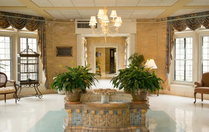 A decorative lobby with a central fountain, plants, and a chandelier.