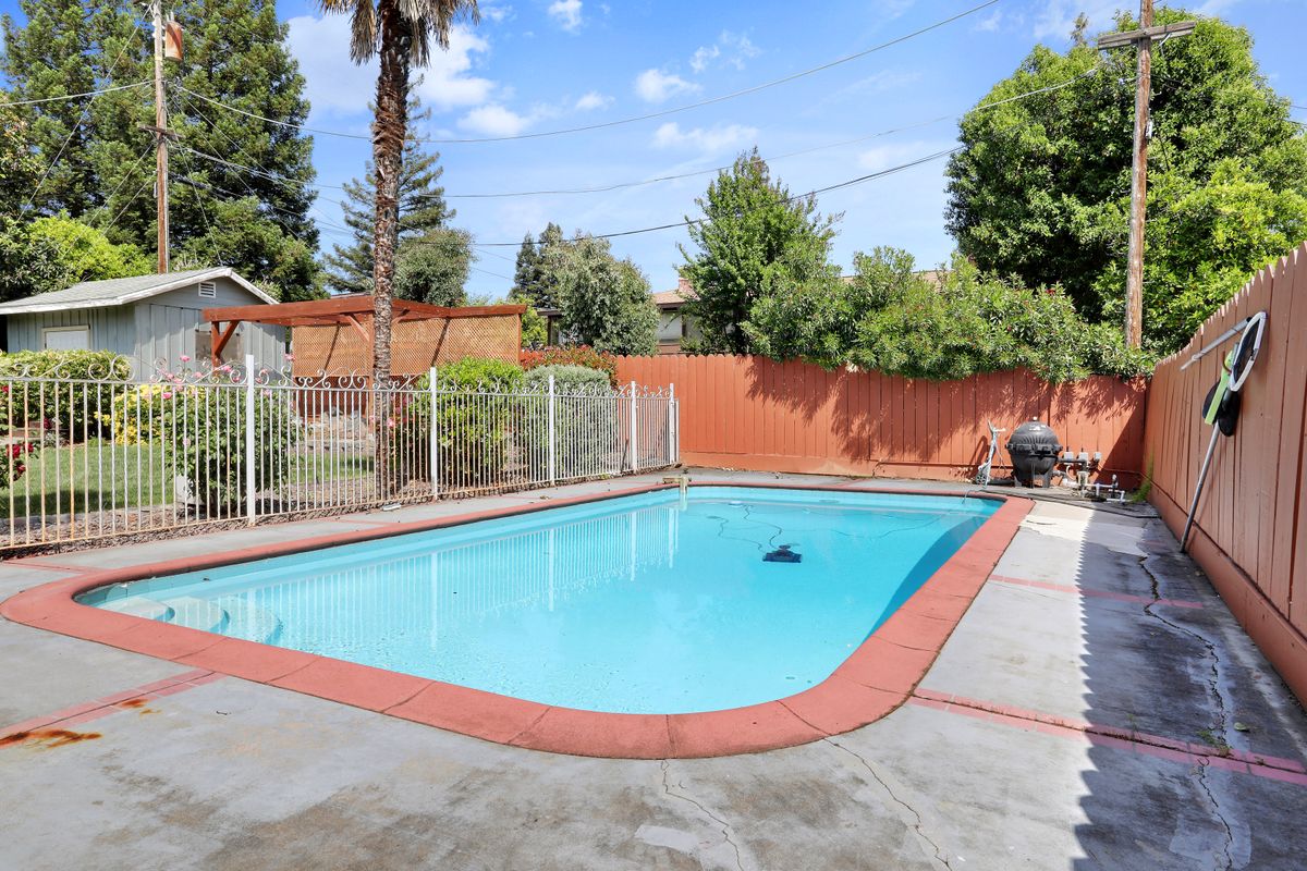 An inviting backyard swimming pool surrounded by a fence and greenery.