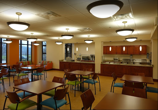 A cozy dining area featuring tables and chairs with a modern design, accompanied by a kitchenette in the background.