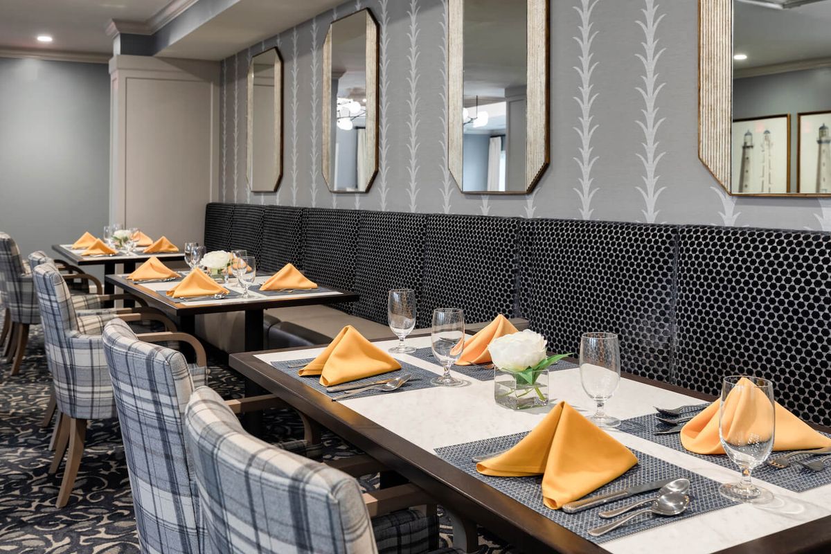 A well-decorated dining area with neatly arranged tables, featuring orange napkins and stylish mirrors.