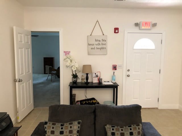 A cozy living room area with a sofa facing a decorated wall featuring a side table, lamp, and wall art.