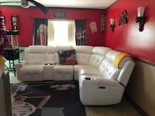 A cozy living room features a white sectional couch against red walls, decorated with wall art and window curtains.
