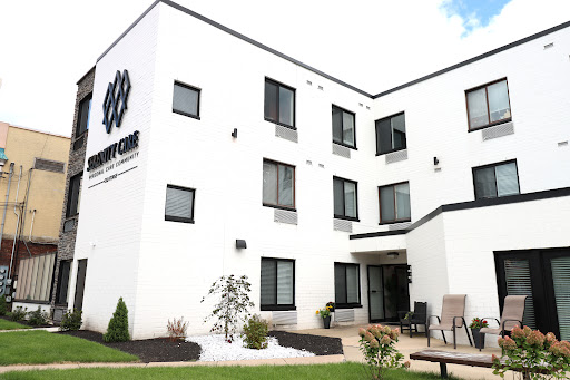 A modern, white building with large windows, featuring a welcoming entrance and landscaped outdoor area.