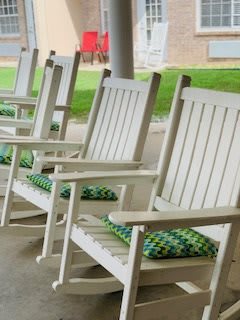 A row of white wooden rocking chairs with green and blue patterned cushions on a porch.
