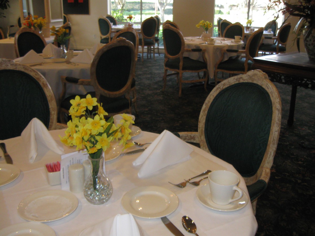 A beautifully set dining table in an elegant restaurant with daffodils as a centerpiece.