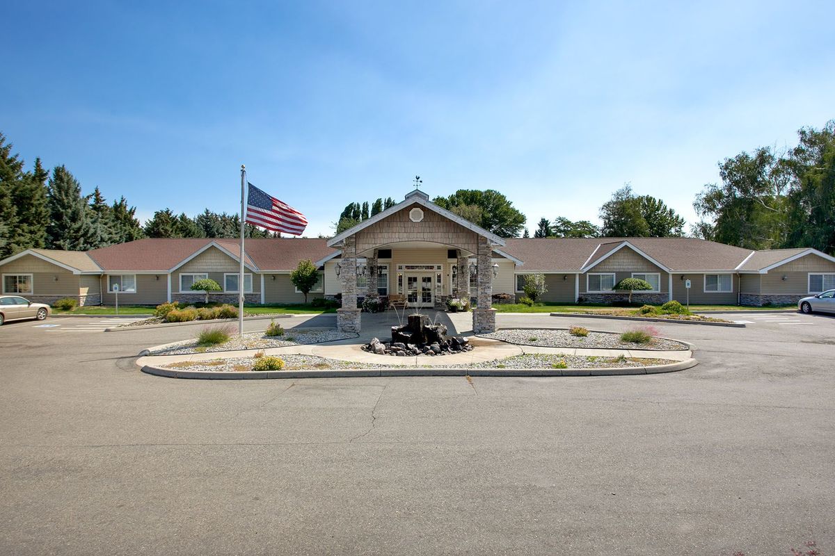 A building entrance with a flagpole in front, surrounded by landscaping on a sunny day.