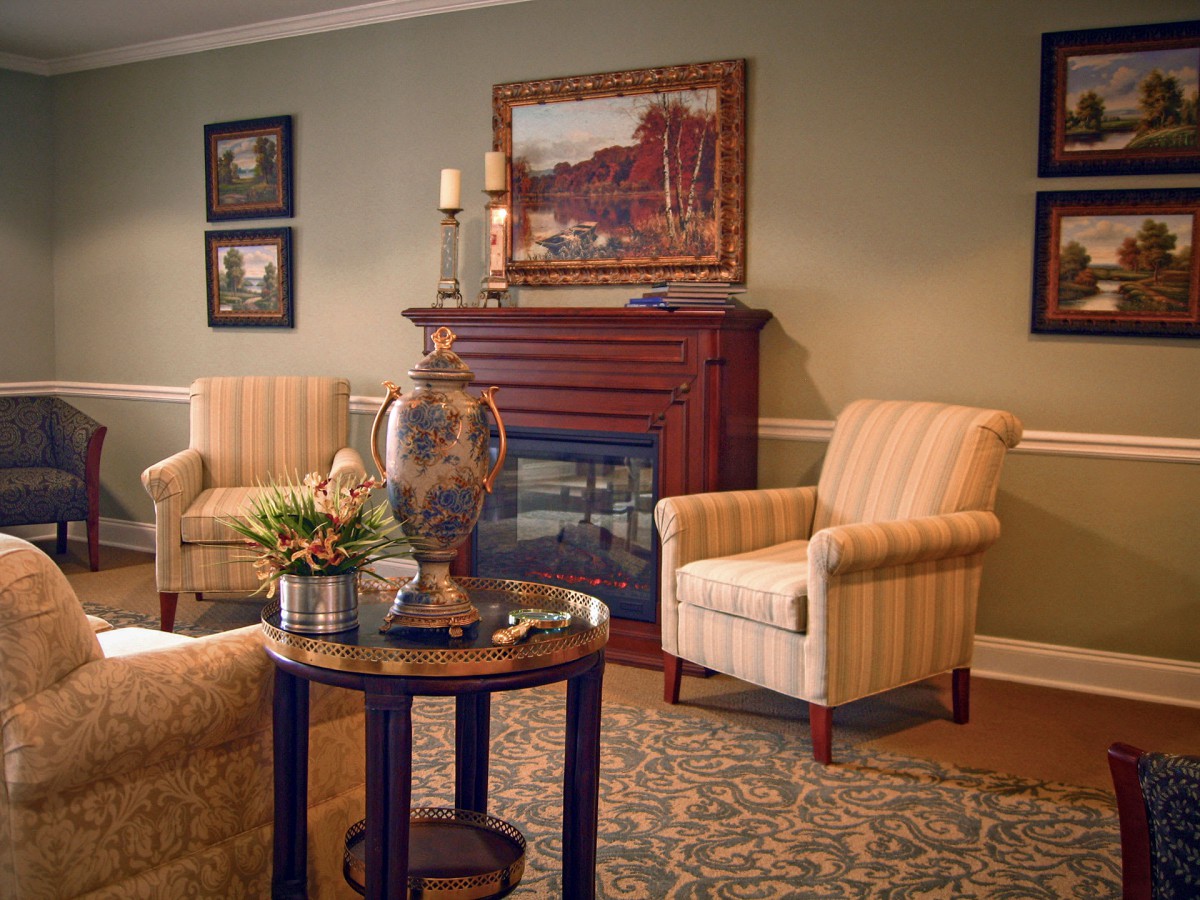 A cozy living room features a traditional fireplace, two striped armchairs, and a round table with a decorative plant.