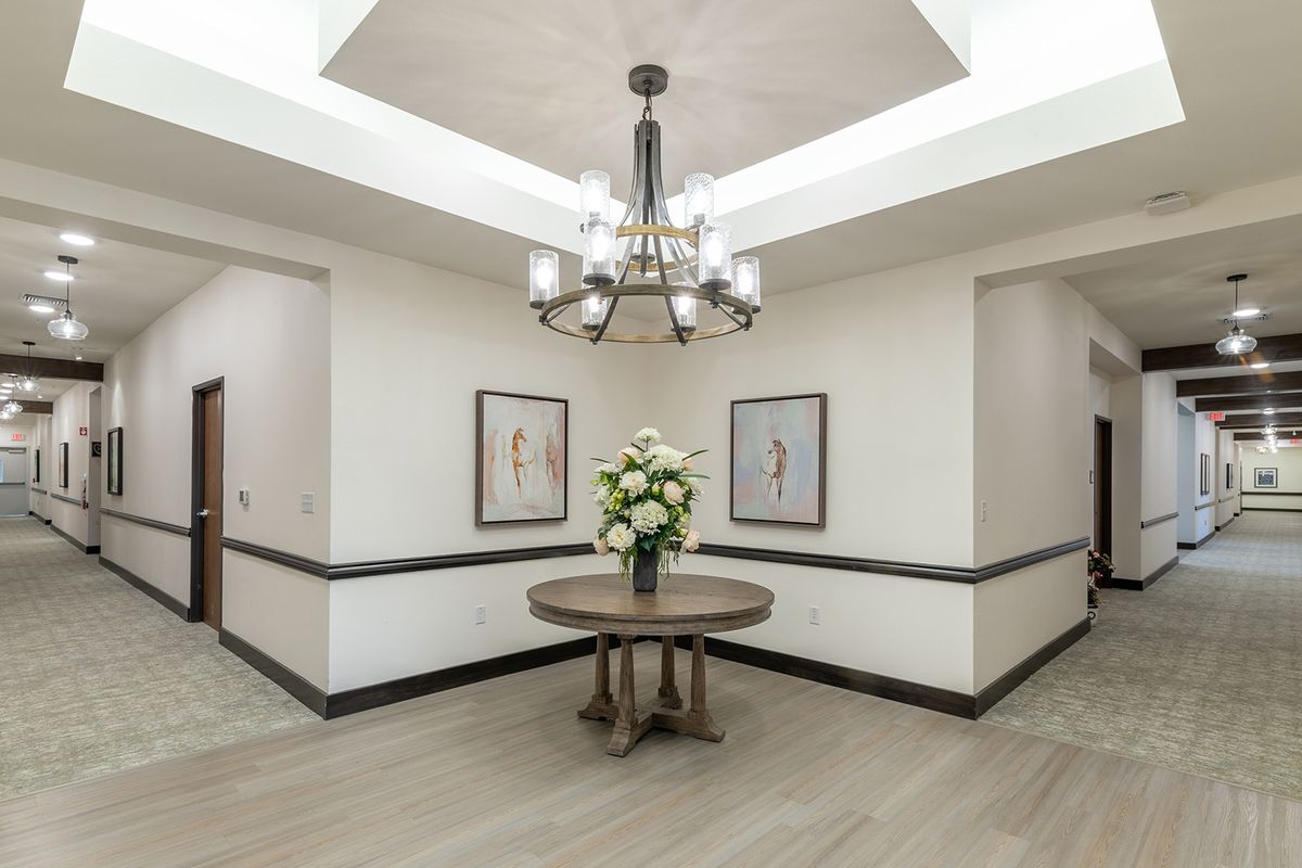 A well-lit lobby area featuring a chandelier, a round table with a floral arrangement, and framed artwork on the walls.
