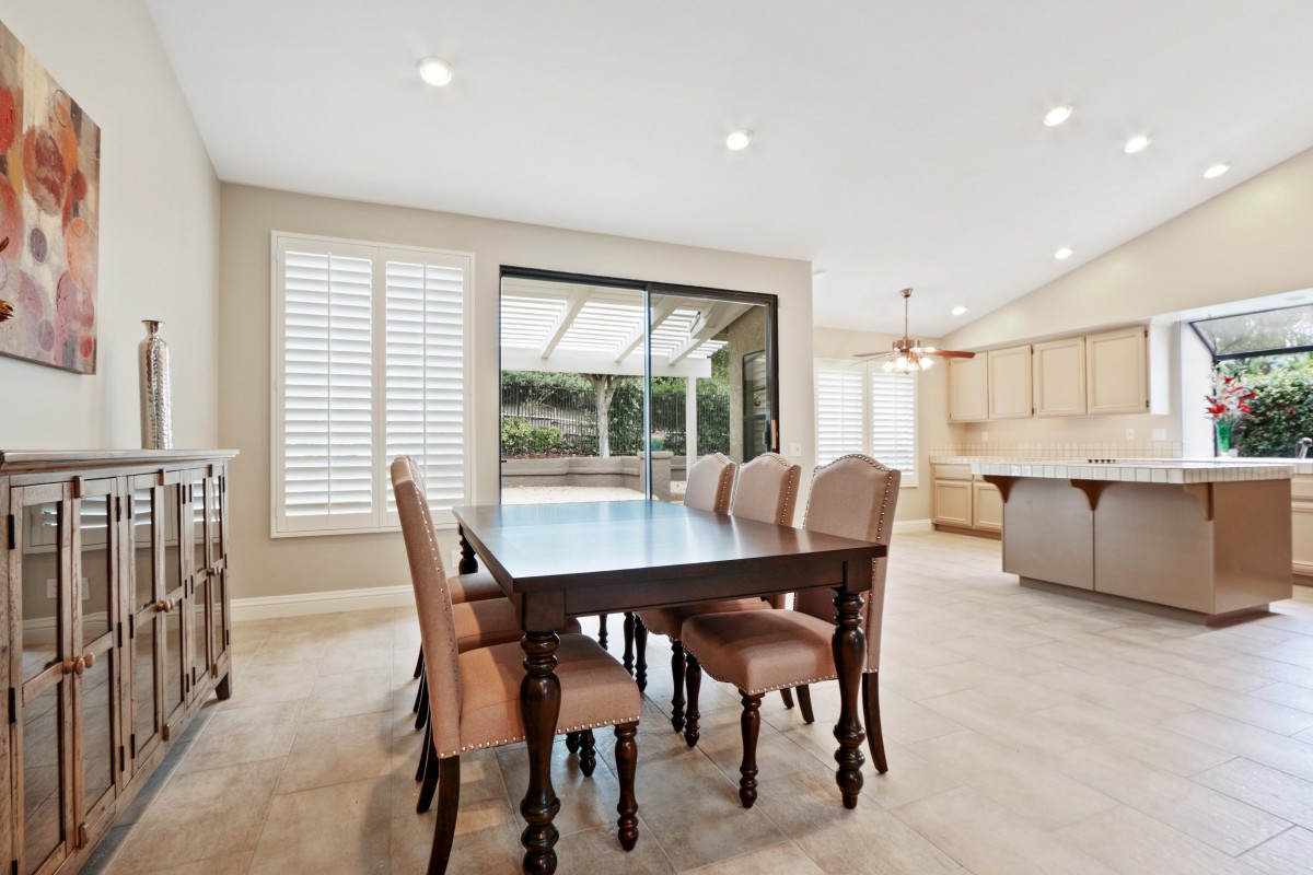 A spacious dining area with a large table and upholstered chairs, overlooking an open kitchen and outdoor patio.