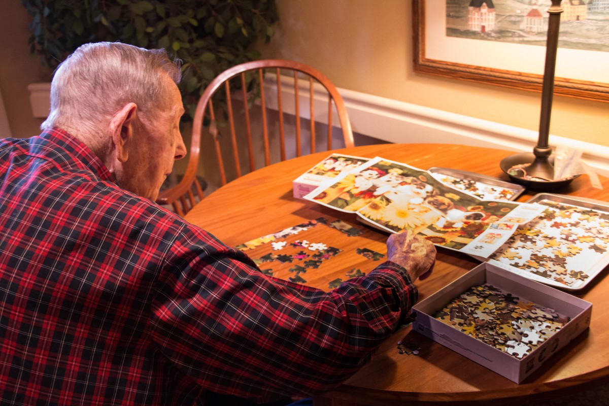 An elderly person working on a puzzle at a table indoors.