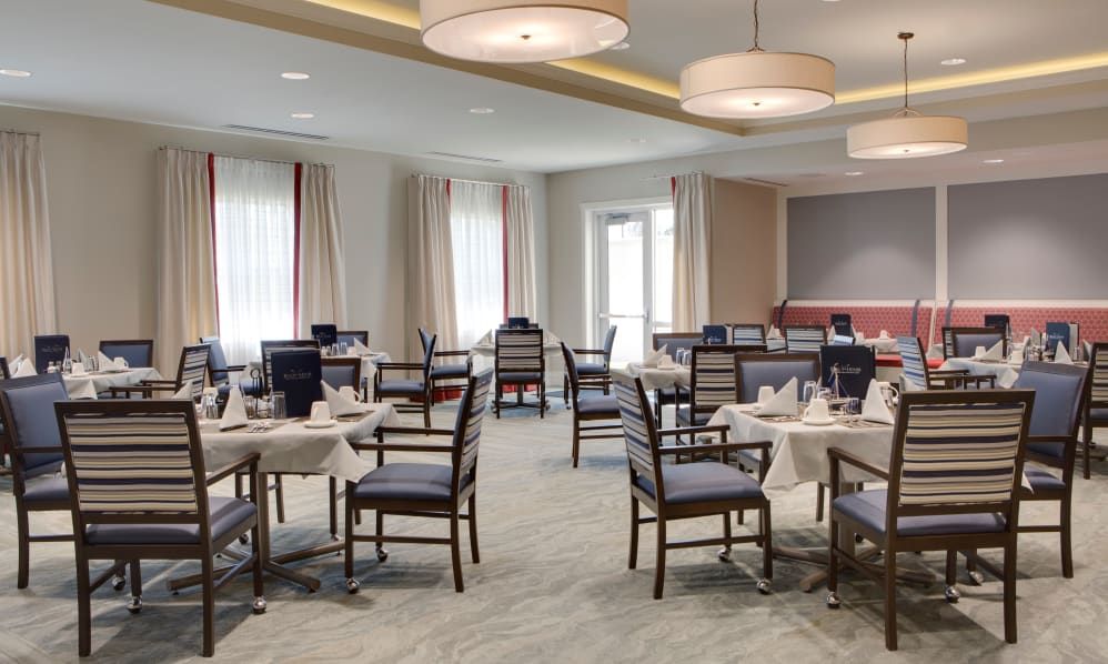 An elegant dining room setup with neatly arranged tables and chairs, featuring soft lighting and large windows.