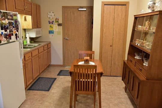 A cozy kitchen with wooden cabinets, a small dining table, and chairs on a linoleum floor.