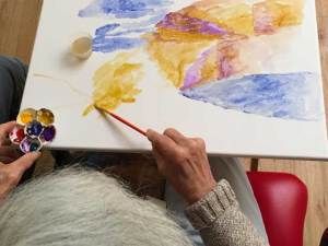 An artist painting with watercolors on a canvas.