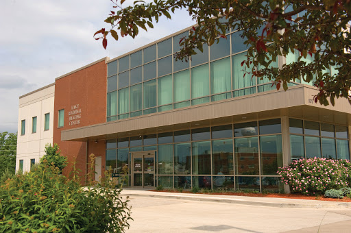 A modern brick building with large glass windows, surrounded by greenery.