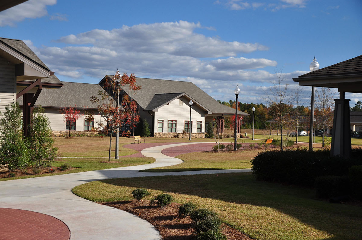 A scenic view of a building surrounded by landscaped lawns and a curved pathway under a partly cloudy sky.