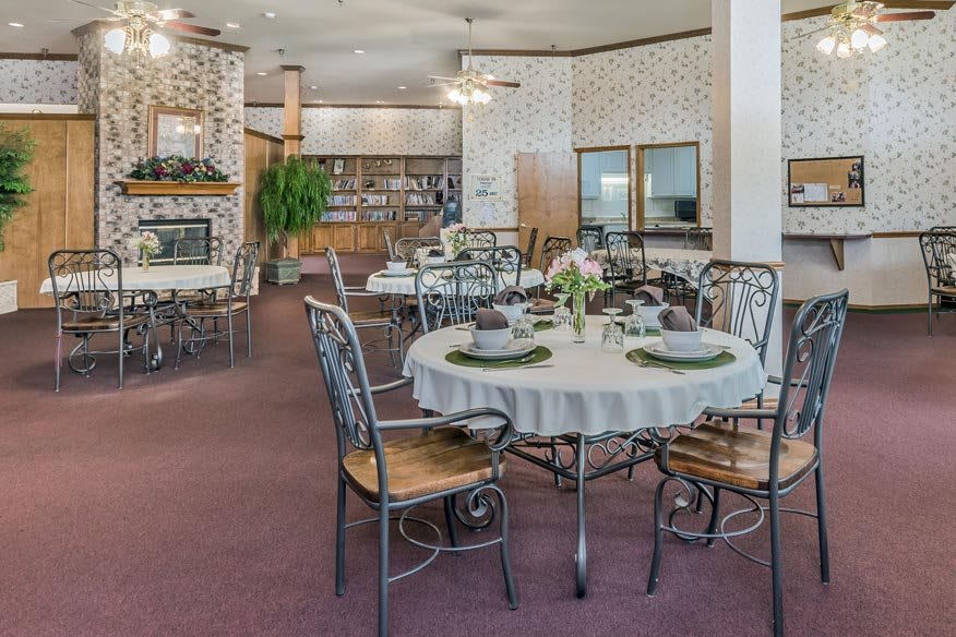 A cozy dining area with elegantly set tables, featuring a warm fireplace and lush greenery.