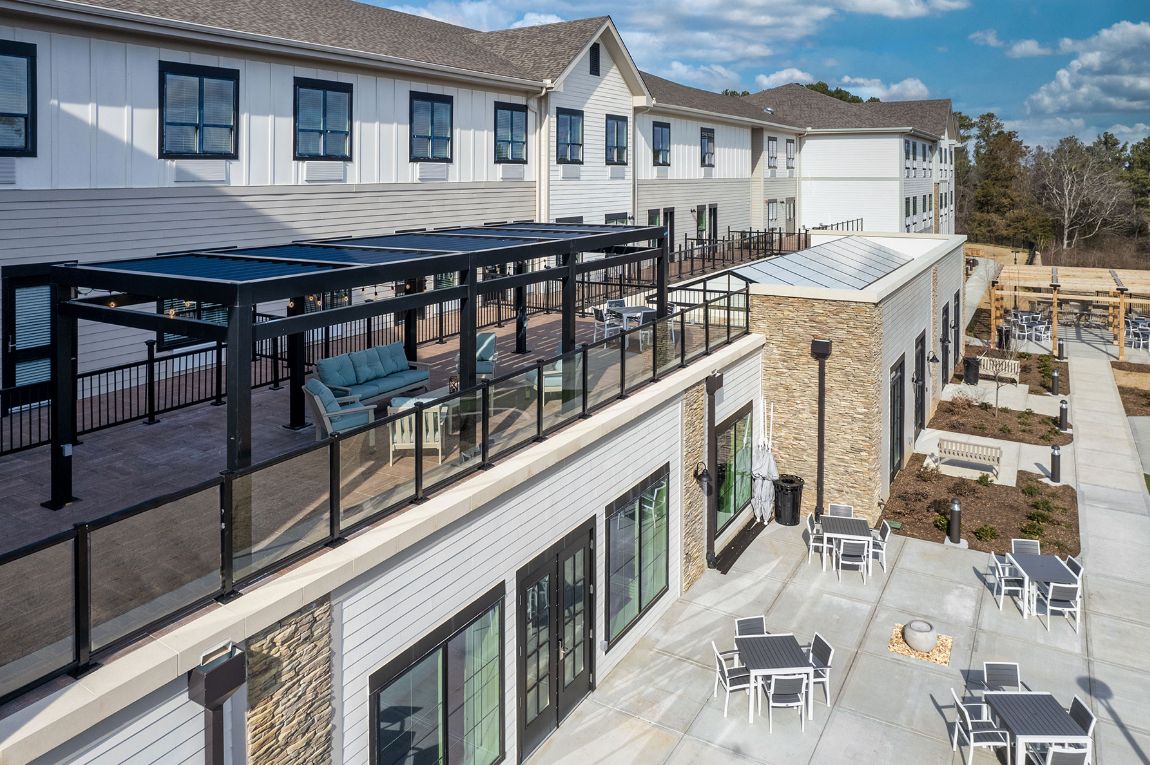 A modern commercial building with outdoor seating and a glass railing on the upper level.