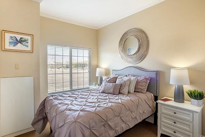 A cozy bedroom with a neatly made bed, featuring a decorative mirror and a lamp near the window.