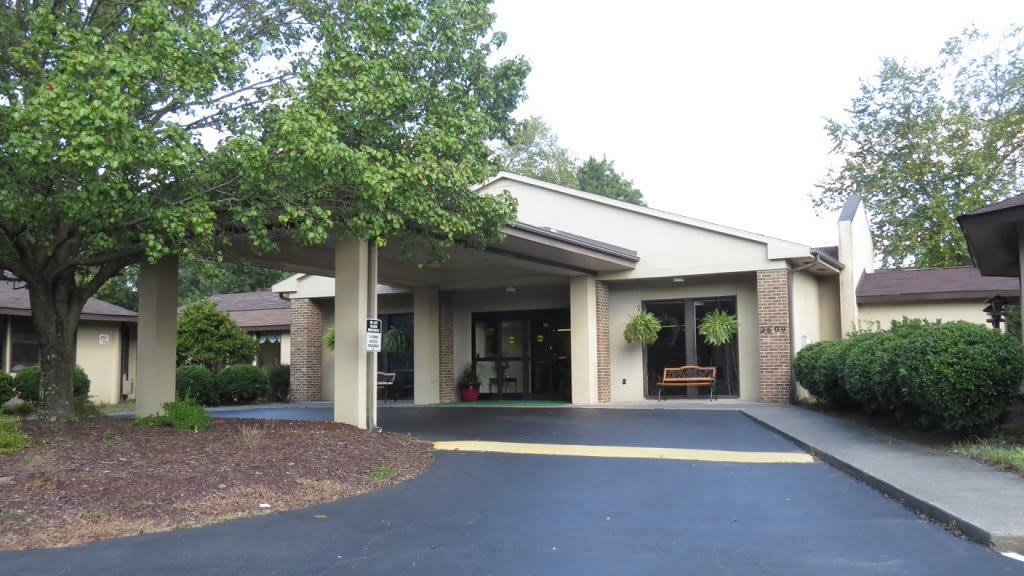 A building entrance with a covered walkway, surrounded by trees and landscaping.