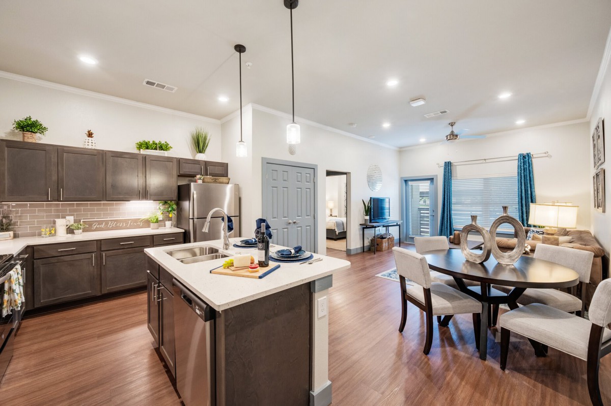 A modern open-concept kitchen and dining area featuring pendant lighting and wood flooring.