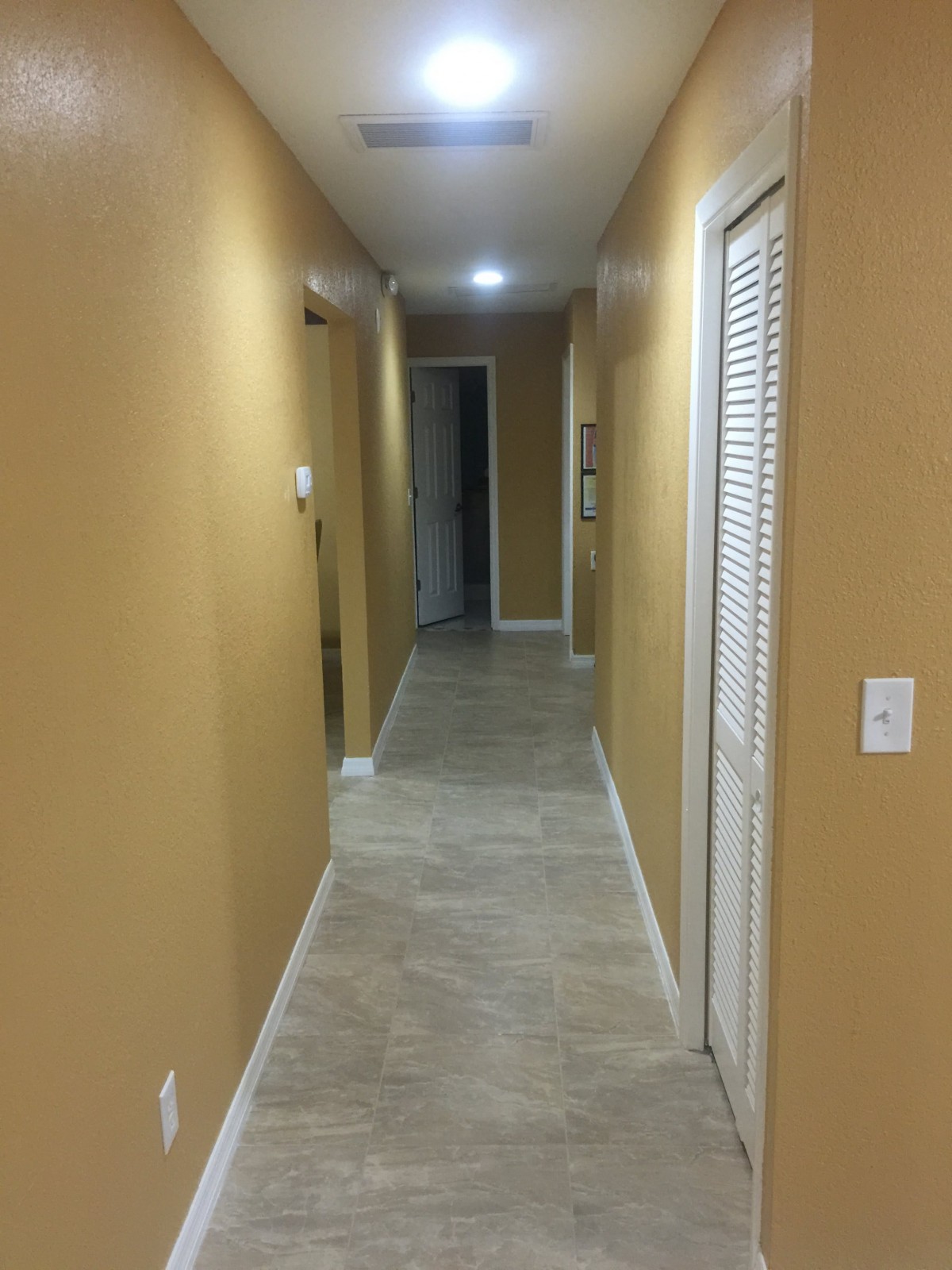 A well-lit hallway with doors on either side and tiled flooring.