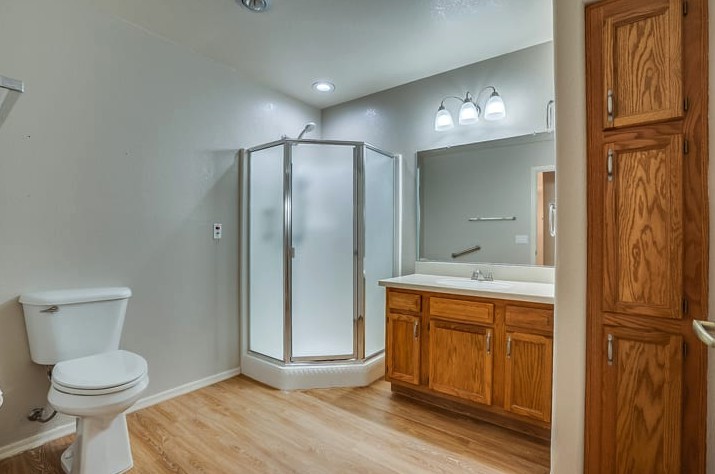 A modern bathroom with a glass shower enclosure, wooden cabinets, and a large mirror.