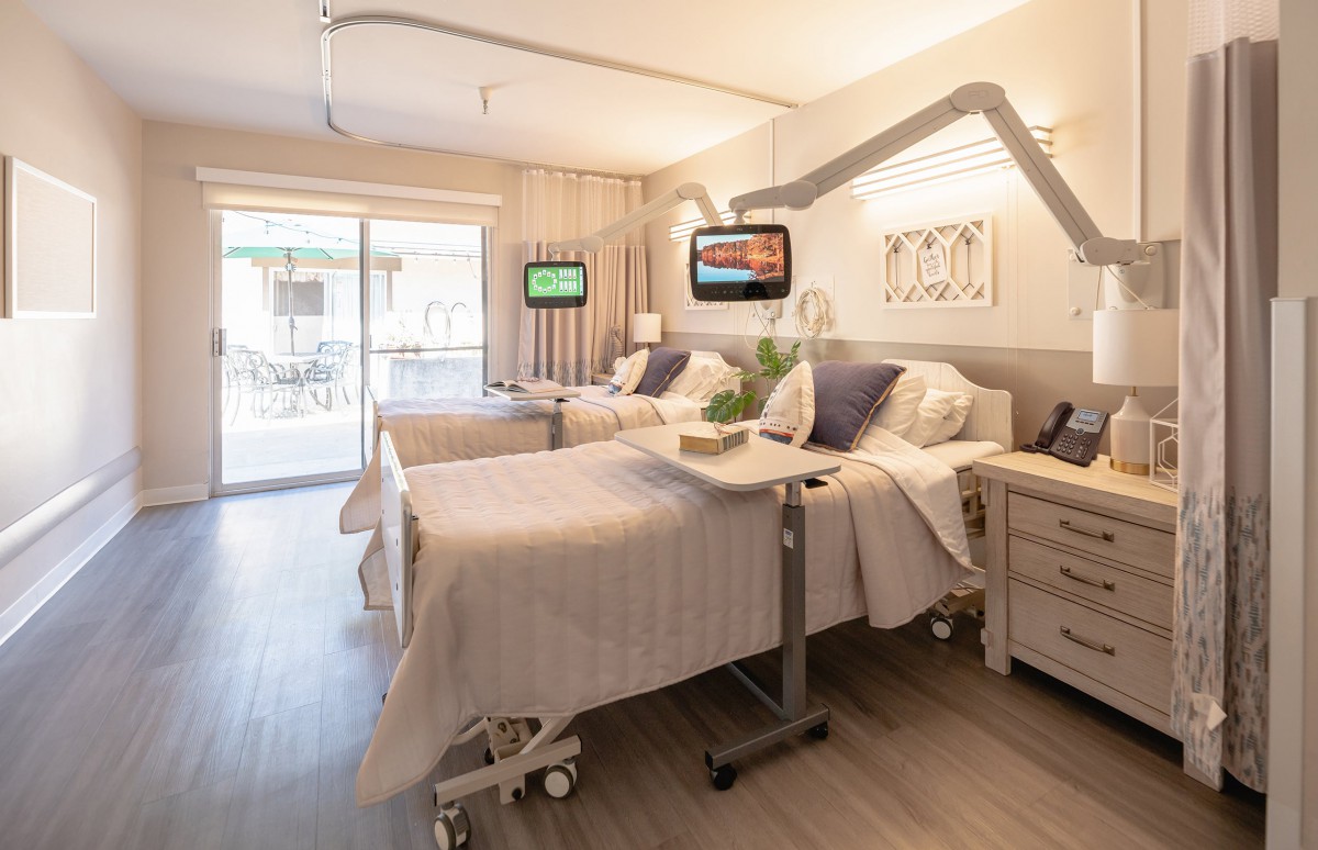 A modern hospital room with two beds, equipped with televisions and medical equipment, designed for patient comfort.