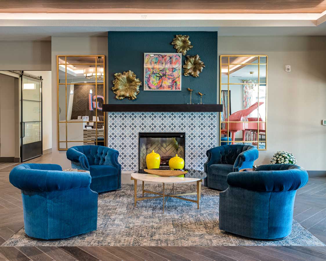 A modern living room featuring a central fireplace surrounded by blue armchairs and decorative elements.